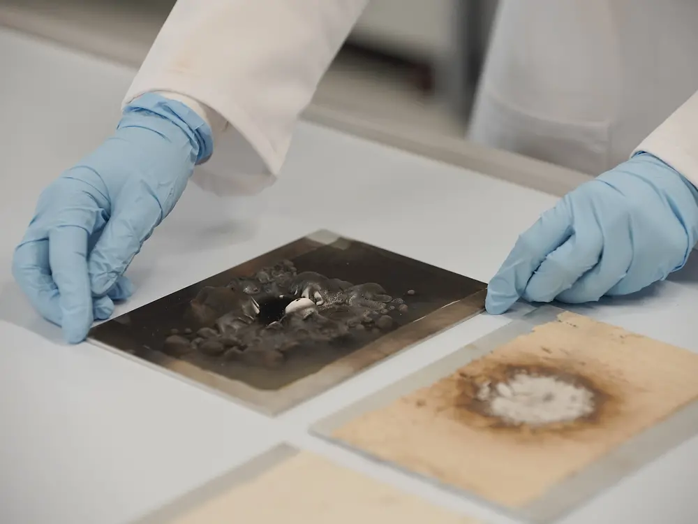 Lab technician examining the results of an open flame test on 2 metal sheets, one coated with Loctice EA 9400, whereas the other is coated with Loctite FPC 5060.